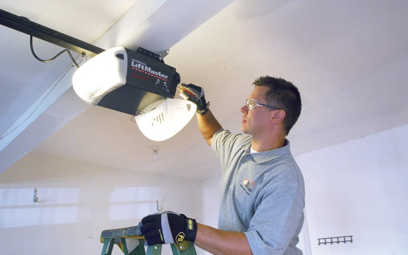 Technician installing a belt drive garage door opener from a step ladder