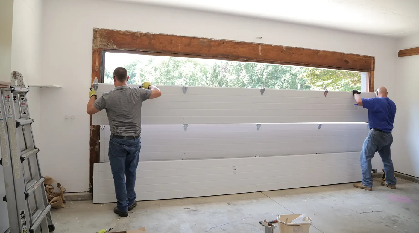 Two fitters setting garage door panels into a new opening during an installation