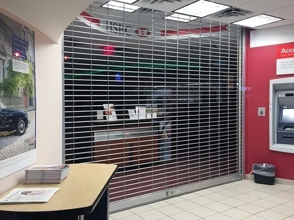 An aluminium rolling closure drawn across a bank branch lobby beside the ATM