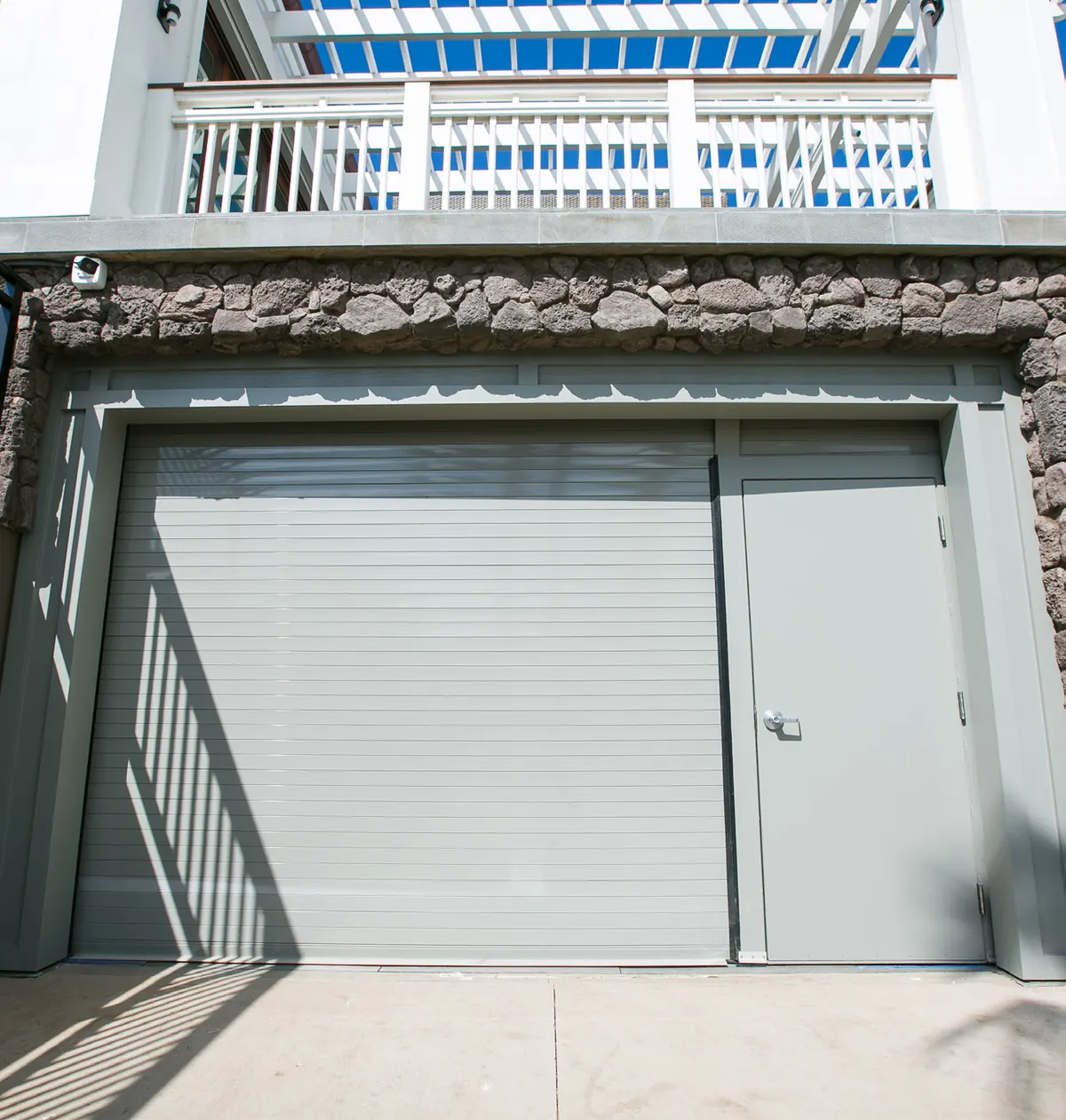 Puerta enrollable de servicio con tablillas de aluminio, pintura en polvo gris, junto a una puerta peatonal en un edificio costero