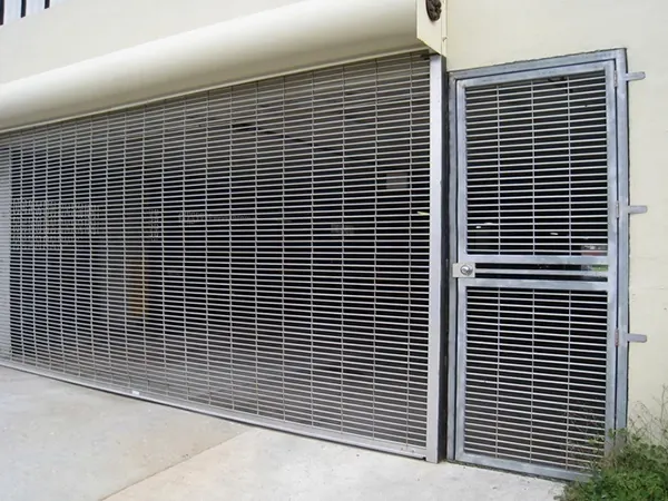 A rolling grille closed across a building front beside a matching pass door