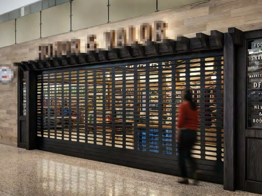 Una puerta enrollable perforada negra cerrada frente a una tienda en un terminal de aeropuerto
