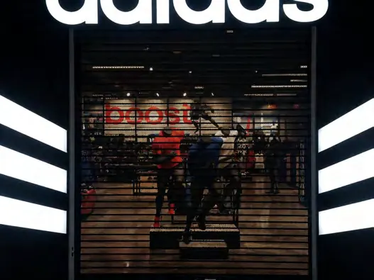 Una puerta enrollable perforada cerrada sobre una tienda de ropa deportiva, con la vitrina iluminada detrás