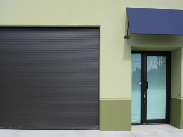 A black steel rolling door beside an entrance with a blue awning